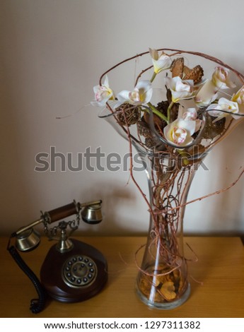 old wood classic phone and a glass vase with fake flowers in a wooden desk and a white wall