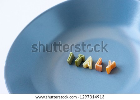 The word "Italy" composed with real pasta letters in the italian flag colors in a blue dish. Background with copy space on the left.