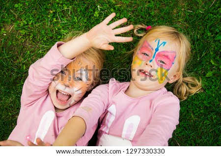 two little girls with colorful painted faces having fun on grass