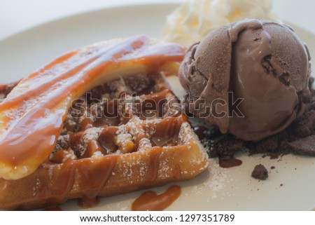 Close up delicious waffle topping with banana and caramel syrup and decoration with chocolate ice cream and whipped cream.