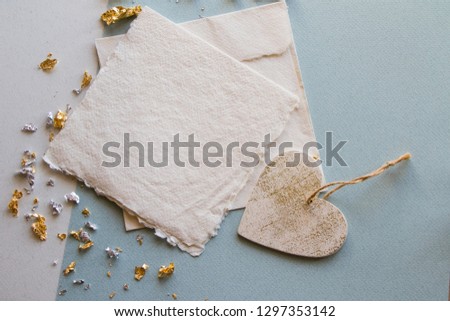 Blank handmade paper note invite with envelope on blue background with white heart and gold flakes, wedding invitation, valentine's day 