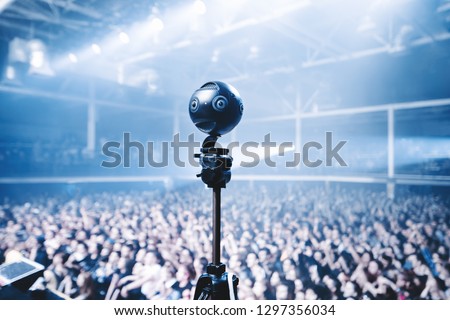 Professional 360 camera at music concert on a tripod recording performance on video.
silhouettes of crowd in front of bright stage lights. Royalty-Free Stock Photo #1297356034
