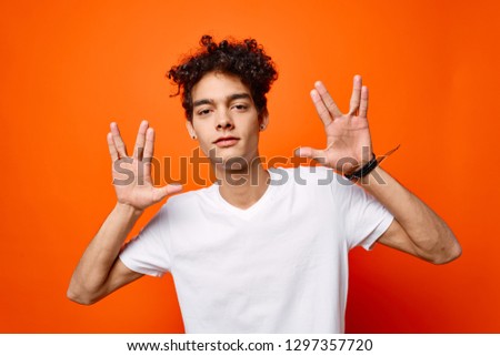 Cute fashionable man with curly hair gesticulates with his fingers on an orange background