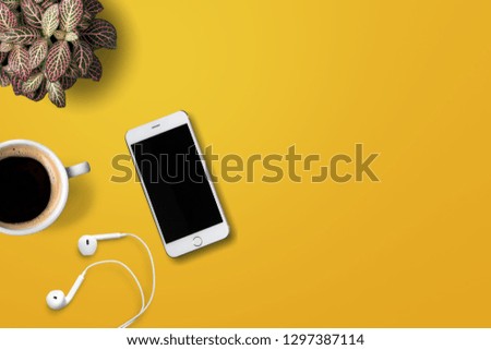 Table top view aerial image of accessories office desk background concept.Flat lay of variety object the white mobile phone & tree pot and coffee with earphone on modern rustic yellow paper and space.