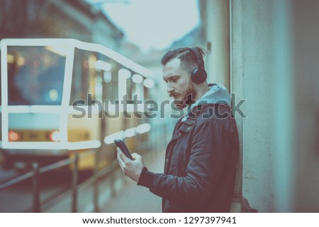 A retro style photo of a hipster man while checking his smartphone in an urban environment.
