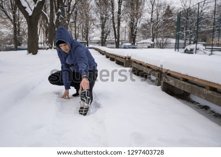 Young man stretching before running at the snow track