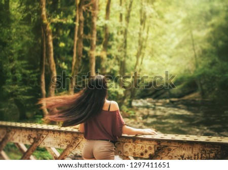 magnificent photo in motion, slim attractive girl waving flying dark light hair, stands on a bridge over a cold transparent river in Georgia, fascinating gorgeous nature is bright and juicy