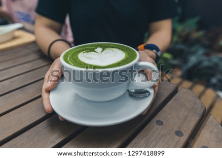 Asia female hand hold cup of matcha green tea latte on Wooden table.