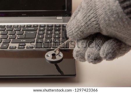 Concept image on the theme of data security with a gloved hand inserting a key into a lock on a laptop computer.