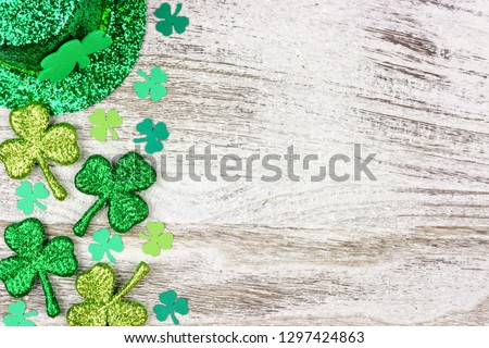 St Patricks Day side border of shamrocks with leprechaun hat over a rustic white wood background