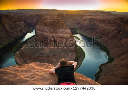 Young man takes smartphone sunset panorama picture of Horseshoe Bend  - water meander made by the Colorado River in Arizonian red rock scenic desert landscape, close to town Page, Arizona, USA.