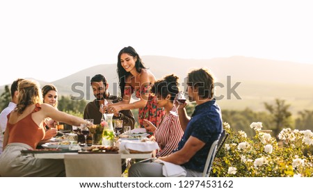 Woman serving food to friends at dinner party. Group of young people having a dinner together outdoors.