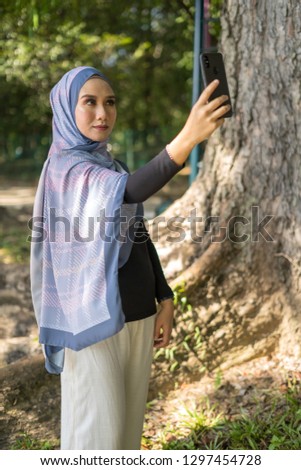 Happy young Asian woman take selfie with her smartphone at blurred park background.
