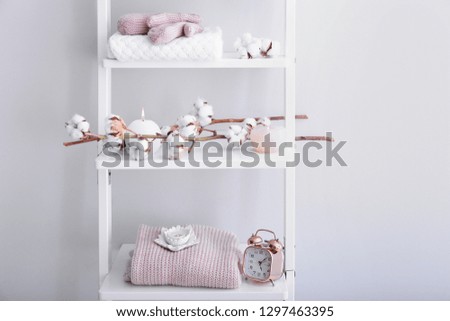 Warm clothes, cotton flowers and candles on shelves near light wall