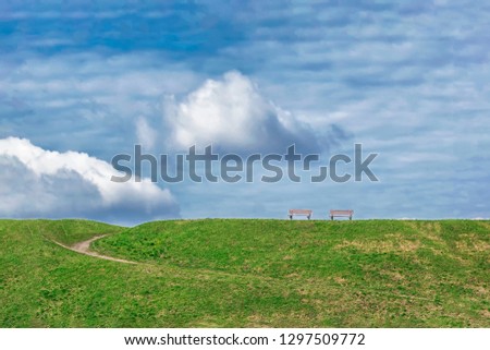 Peaceful picture of two wooden benches on the top of the hill with beautiful blue sky and clouds