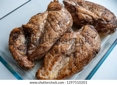 Three roasted chicken breasts with salt and black pepper in a glass container. Macro picture.