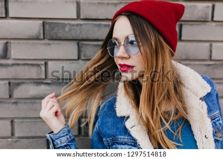 White blonde girl with trendy makeup playfully posing on urban background. Portrait of good-looking young woman in denim jacket spending time outdoor.