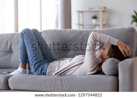 Sad depressed young woman lying on couch at home feeling headache fatigue loneliness, upset tired sick ill teen girl suffer from migraine anxiety, drowsy somnolent teenager rest on sofa after stress Royalty-Free Stock Photo #1297544821