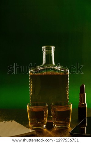 Bottle glass with whiskey and lipstick on a green green background.