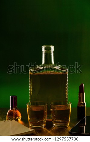 Bottle glass with whiskey and lipstick on a green green background.