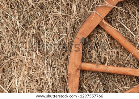 wooden wheel leaning against a stack of dry hay