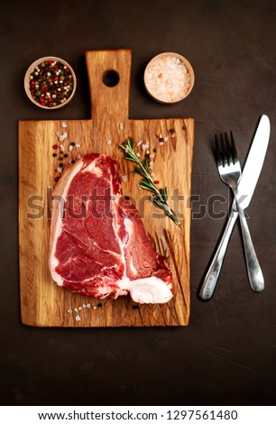 
Raw meat steak with seasoning on a cutting board, background concrete. . Beef T-bone steak, top view. Barbecue concept. Ingredients for roasting meat.