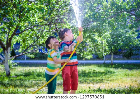 Brothers having fun splash each other with water in the village. Boys having fun with watering fruit garden in village outdoors. Funny holiday leisure water for children. Royalty-Free Stock Photo #1297570651