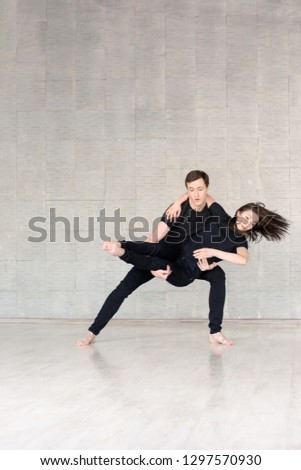 Young couple in black dancing. Dancers in action over grey background. Talented young man and woman practising new dance.