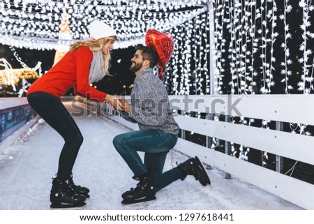 Handsome man proposing a beautiful woman to marry him in ice skating rink.