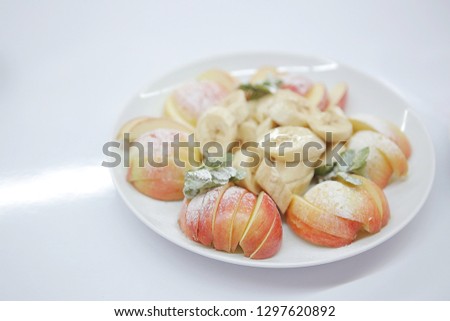 Dish with sliced ​​apple and banana and powdered sugar. Healthy dessert on white background