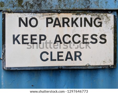 Slightly rusty No Parking Keep Access Clear sign attached to a blue corrugated metal fence / gate