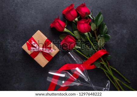 Red rose flowers bouquet, gift box, champagne glasses on black stone background Valentine's day greeting card Copy space Top view