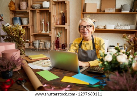 Portrait of smiling female small business owner using laptop and looking at camera in flower shop, copy space