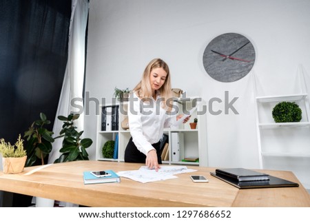 Theme business woman at work. Beautiful young caucasian woman business man working standing in the office near the table, checks edits financial charts on paper.