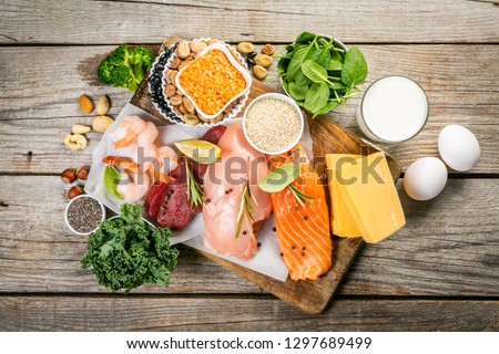Selection of animal and plant protein sources - fish, meat, beans, cheese, eggs, nuts and seeds, kale, on wood background Royalty-Free Stock Photo #1297689499
