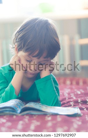 The boy lies on the couch and looks at the picture in the book.