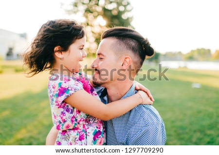 Closeup portrait of happy smiling father holding, hugging, playing, having fun with his cheerful laughing, smiling funny pretty daughter outdoor in summer.  Dad loves his female child. Family in park