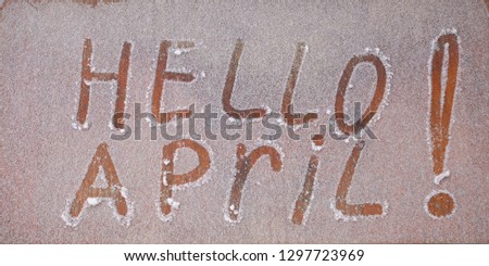 The inscription "Hello April!" on wooden background. Letters in the snow.