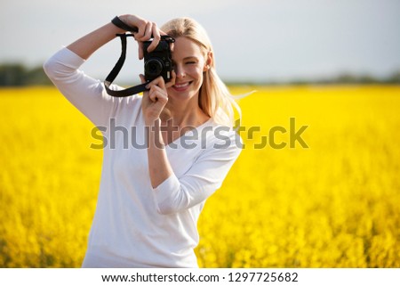 Young woman with camera taking a photo of rape seed field in flower