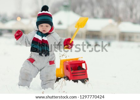 little baby boy playing with his favourite toy at the snowtime. A kid 15-23 month enjoy playfull,spending time in snow. A toddler  and his plastic truck at the winter games. Kids and toys concept.