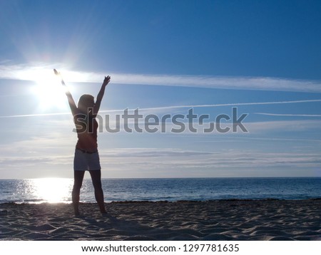 Silhouette of woman with outstretched arms standing on beach