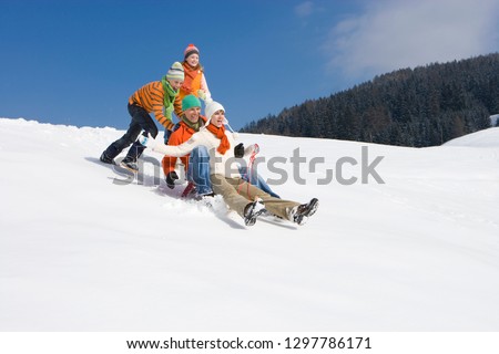 Family winter vacation with children pushing parents on sled down hill