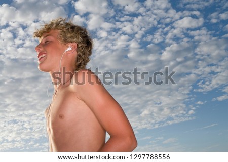 Smiling young boy listening to music on headphones against blue sky