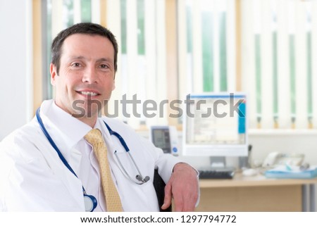 Smiling doctor in white coat with stethoscope in office at camera