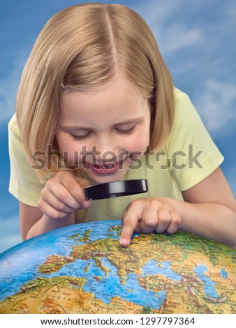 Curious girl with magnifying glass looking at a globe with blue sky