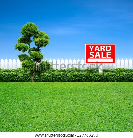 Yard sale sign and white fence on green grass
