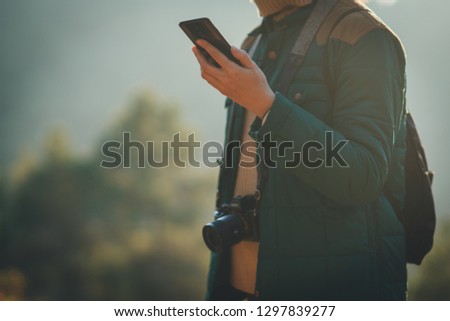 Crop picture of traveller girl with a photo camera holding cell telephone and checking the road in online map, copy space for your text and logo, blurred nature, trees and forest in the background