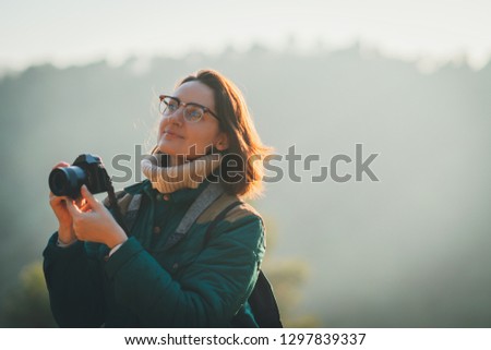 Happy smiling female photographer taking pictures of nature and birds on her camera while travelling around the forest in the mountains, copy space for text