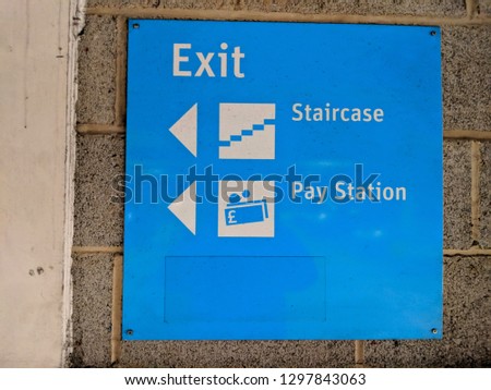 Bright blue exit sign in a car park with directional arrows to the staircase and the pay station