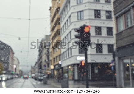 Cold rain. Wet snow in the city. Drive. Poor weather conditions. Red traffic light. Overcast. Rainy backdrop. Bad visibility on roads. Perspective. Blurred avenue scene. Blur urban background.